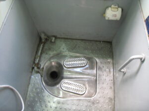 Squat toilet on the train with grab bar. White hose on bottom left is the vietnamese bidet.